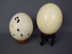 LOT WITHDRAWN - Two blown ostrich eggs (Struthio camelus), one with carved decoration, on stands.