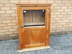 A pine cupboard with single glazed door, approximately 91 cm x 64 cm x 26 cm.