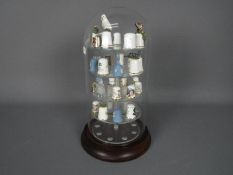 A glass domed display case containing approximately 30 thimbles to include a silver hall marked