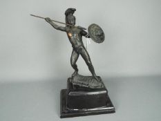 A cast metal sculpture depicting a Greek warrior with shield throwing a spear,