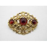 A 14ct gold openwork scroll brooch set with three red cabochons, approximately 12 grams all in.