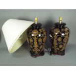A large pair of ceramic table lamps with stylised floral decoration against a black ground,