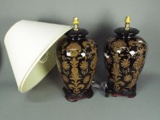 A large pair of ceramic table lamps with stylised floral decoration against a black ground,