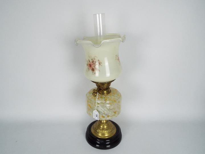 An oil lamp with black ceramic base and brass support below a mottled glass reservoir and floral