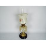 An oil lamp with black ceramic base and brass support below a mottled glass reservoir and floral