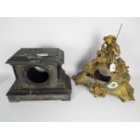 Two mantel clock cases, one a figural brass example, the other black slate with gilt highlights,