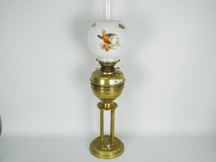 A brass oil lamp on circular base with four column supports, the shade decorated with game birds,