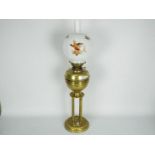 A brass oil lamp on circular base with four column supports, the shade decorated with game birds,