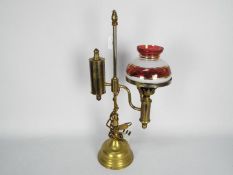 A brass desktop oil lamp (converted) with red and white glass shade with gilt highlights,