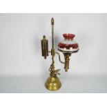 A brass desktop oil lamp (converted) with red and white glass shade with gilt highlights,