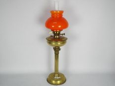 A brass oil lamp with fluted column support and orange glass shade,