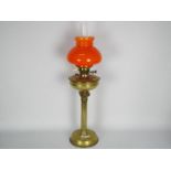 A brass oil lamp with fluted column support and orange glass shade,