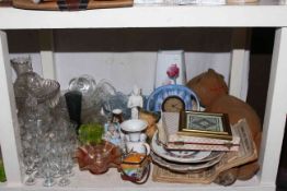 Full shelf of glassware, metalwares, vintage teddy, stone jar, brassware, etc.