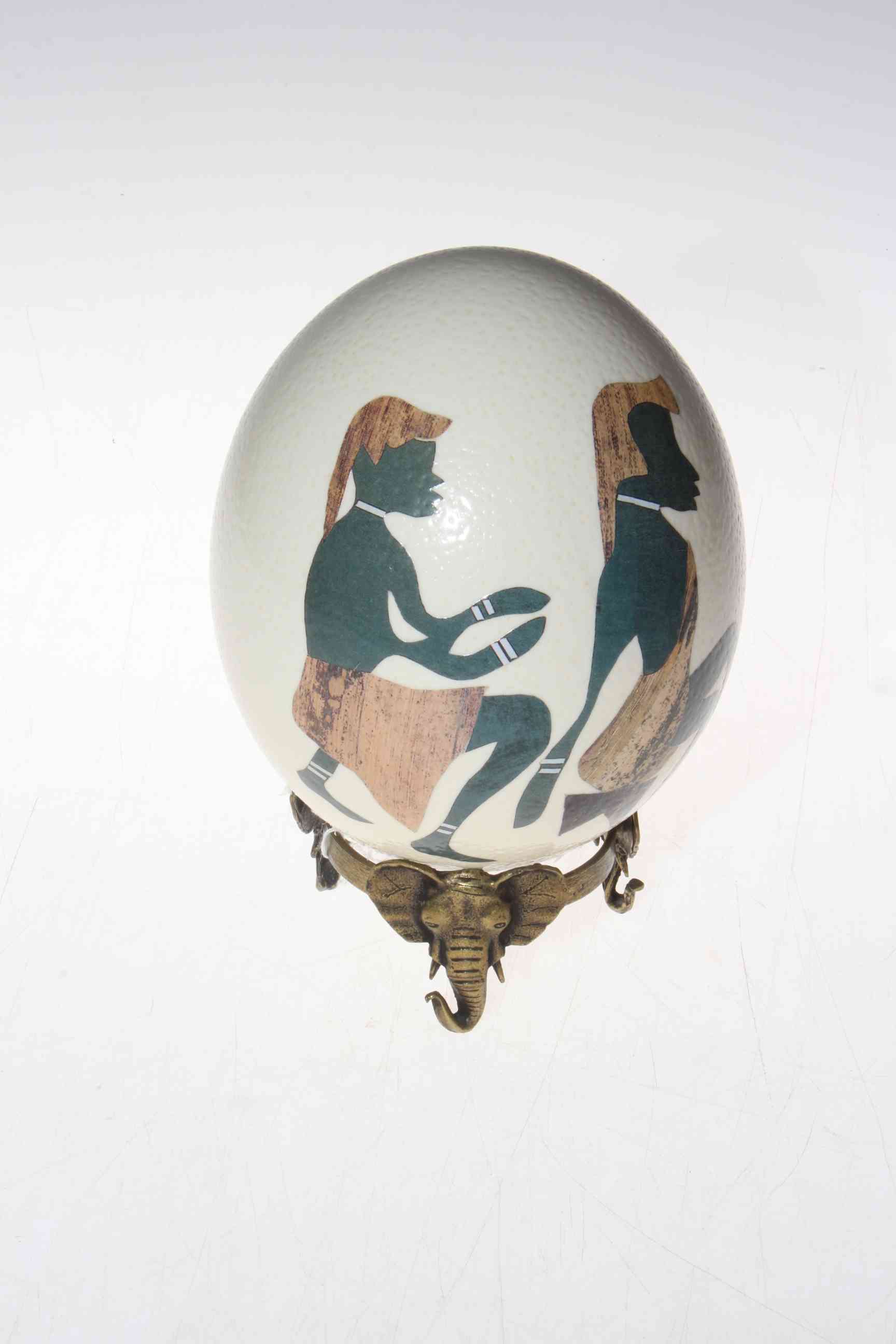 Ostrich egg decorated with figures on metal elephant mask stand.