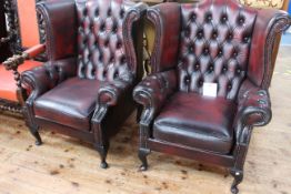 Pair ox blood buttoned leather wing back armchairs on cabriole legs.