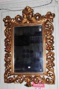 Ornate gilt framed bevelled wall mirror, 125cm by 84cm overall.