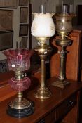 Three oil lamps, one with etched cranberry glass shade and two brass column oil lamps,