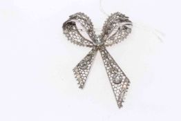 Diamond set filigree ribbon brooch set in white metal (most likely gold or platinum),