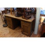 Edwardian oak pedestal desk having five drawers and panelled door cupboard,