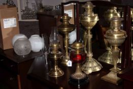 Collection of five brass oil lamps, one with ruby reservoir, four chimneys and three shades.