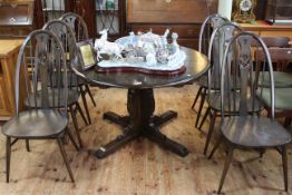 Ercol dark elm circular extending dining table and six swan back chairs.