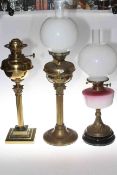 Three vintage brass columned oil lamps, two with shades and one with a pink reservoir.