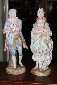 Pair of tall bisque porcelain figures in Regency costume, standing against tree stumps,