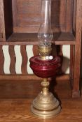 Victorian brass columned oil lamp with red glass reservoir.