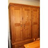 Pine combination wardrobe having three panelled doors above two drawers, 214cm by 140cm by 60cm.