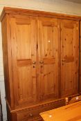 Pine combination wardrobe having three panelled doors above two drawers, 214cm by 140cm by 60cm.