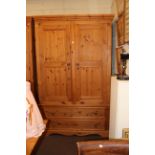 Pine combination wardrobe having two panelled doors above two drawers, 216cm by 135cm by 61cm.