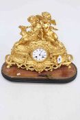 Ornate gilt metal mantel clock surmounted by cherubic figures on wooden stand, 46cm by 40cm.