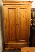 Pine wardrobe having two doors above a base drawer, 209cm by 111cm by 58cm.