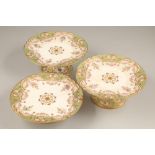 A suite of three painted Copeland jewelled porcelain comports, with hand painted flower decoration