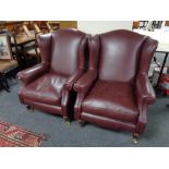 A pair of Victorian style wing backed armchairs upholstered in burgandy leather