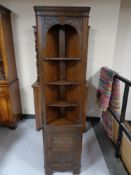 A carved oak corner display stand fitted a cupboard beneath