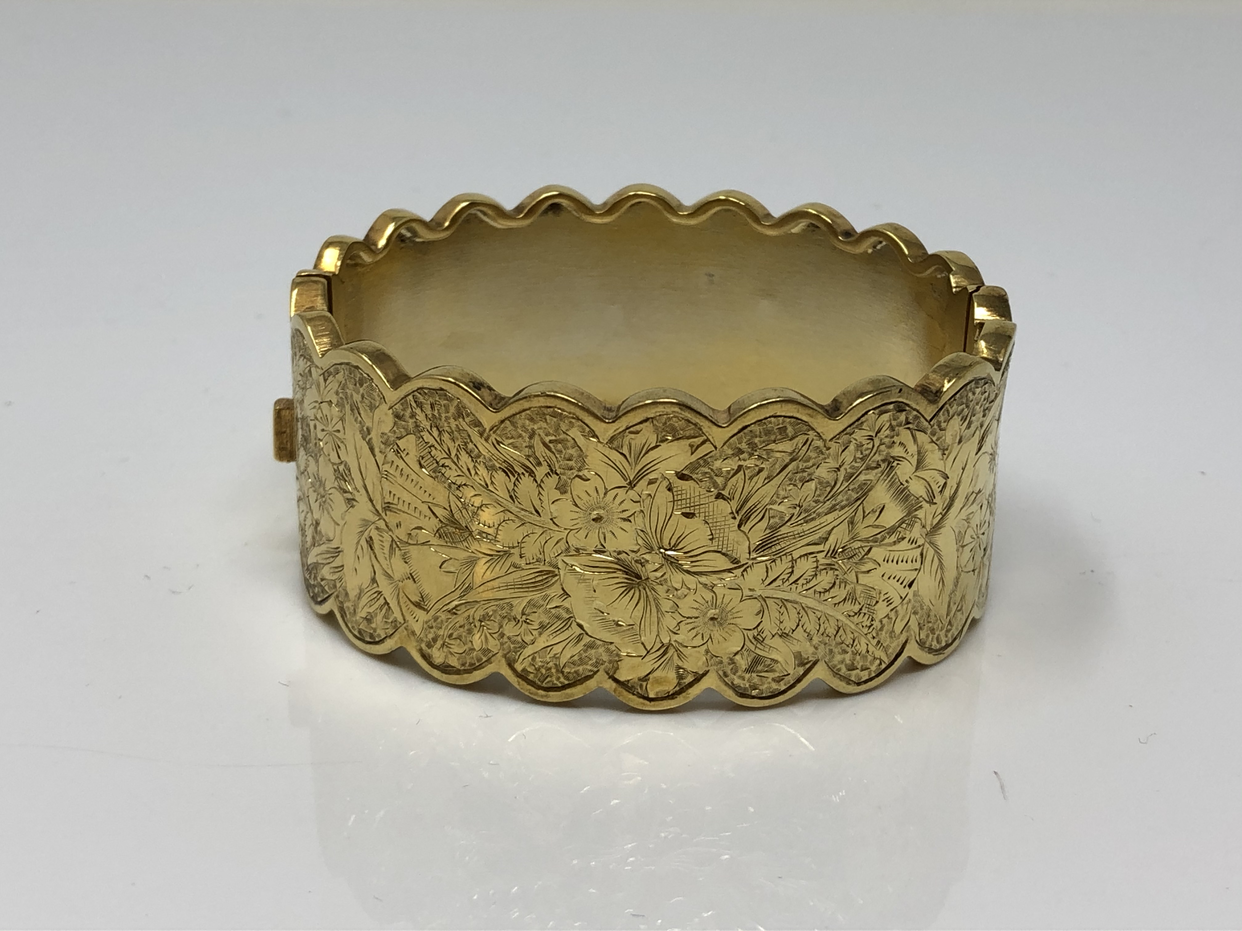 An ornate late Victorian gold plated hinged bangle with engraved decoration