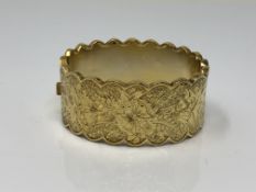 An ornate late Victorian gold plated hinged bangle with engraved decoration