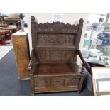 An antique carved oak storage seat, the carved back depicting figures,