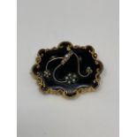A Victorian mourning brooch highlighted with seed pearls on yellow metal and black glass,
