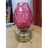 An antique brass paraffin lamp with cranberry glass shade