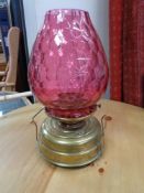 An antique brass paraffin lamp with cranberry glass shade