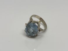 A continental white metal ring, the textured collet set with an oval blue stone, size N/O,