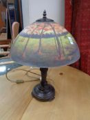 A reproduction table lamp with glass shade depicting a forest landscape