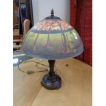 A reproduction table lamp with glass shade depicting a forest landscape