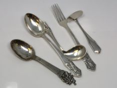 A highly ornate silver spoon and a four piece christening set depicting scenes from folklore signed,