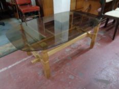 An oval smoked glass topped coffee table on blond oak base