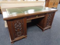 An early 20th century oak twin pedestal desk with carved panel doors and a green tooled leather