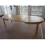 An oval blond oak extending dining table with two leaves