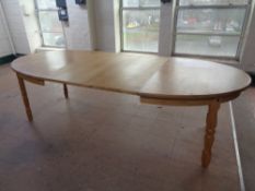 An oval blond oak extending dining table with two leaves